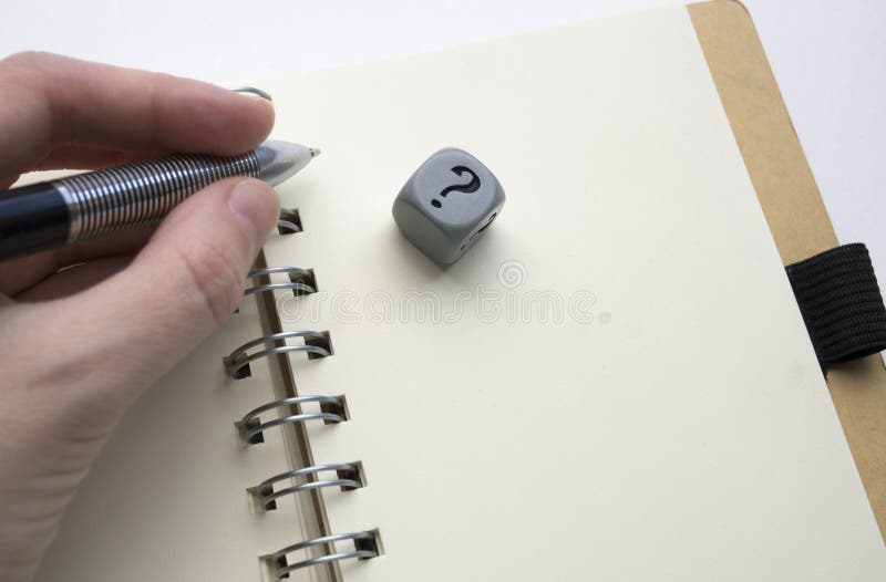 Linkerhand die een pen boven een grijze blanco pagina van een spiraal houden - het verbindende notitieboekje, dobbelt met vraagte stock foto Linkerhand die een pen boven een grijze blanco pagina van een spiraal houden - het verbindende notitieboekje, dobbelt met vraagte stock foto