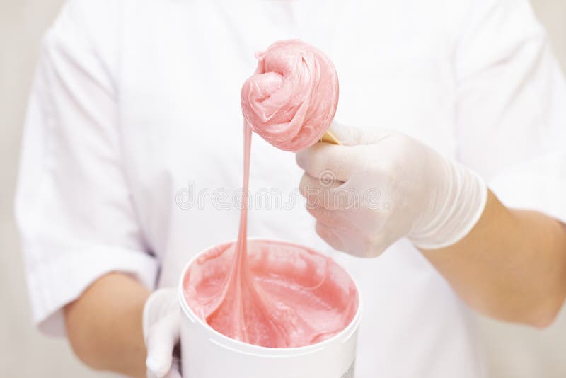 Liquid pink sugar paste or wax for depilation on a wooden stick close up on a white background, against the background of the uniforms of a depilation master. Depilation paste stock images, royalty-free photos and pictures