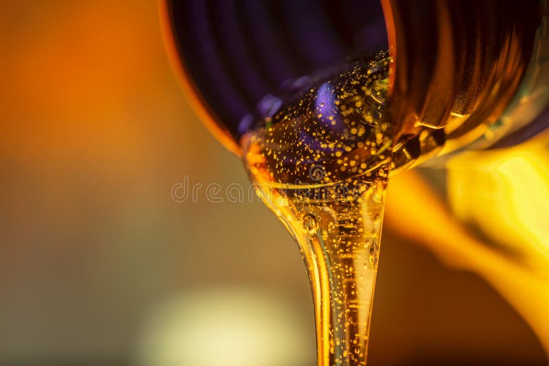 Liquid stream of motorcycle motor oil flows from the neck of the bottle close-up.