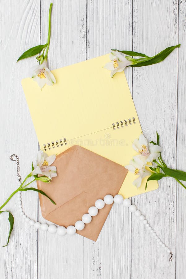 Lis blancs avec le carnet jaune et perles avec l'enveloppe de m?tier sur la table en bois blanche, vue sup?rieure, configuration image libre de droits Lis blancs avec le carnet jaune et perles avec l'enveloppe de m?tier sur la table en bois blanche, vue sup?rieure, configuration image libre de droits