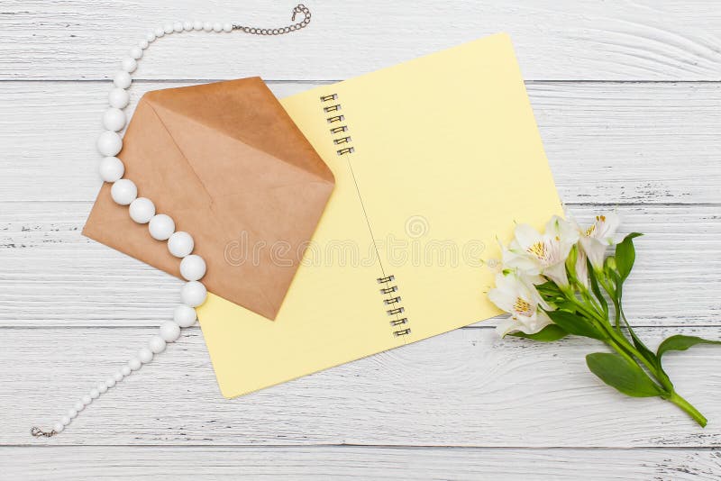 Lis blancs avec le carnet jaune et perles avec l'enveloppe de métier sur la table en bois blanche, vue supérieure, configuratio images stock Lis blancs avec le carnet jaune et perles avec l'enveloppe de métier sur la table en bois blanche, vue supérieure, configuratio images stock
