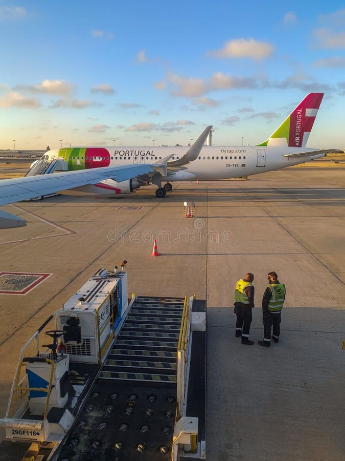 TAP airplane with boarding bridge at Humberto Delgado airport and workers with a tractor delivering luggage to the plane, Lisbon PORTUGAL. TAP airplane with boarding bridge at Humberto Delgado airport and workers with a tractor delivering luggage to the plane, Lisbon PORTUGAL