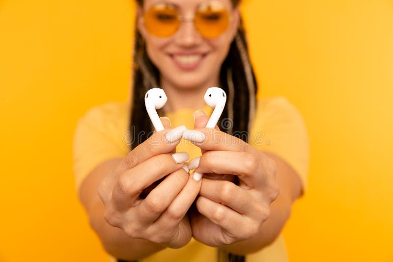 Listening music on airpods. Woman in the yellow studio with white airpods.