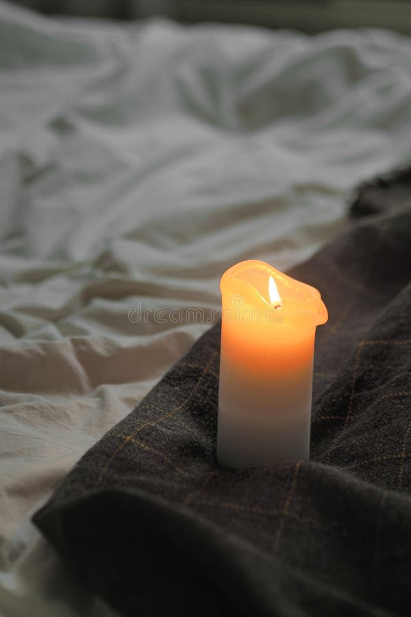 A Lit Candle Sitting on a Blanket Thats Covered in Wrinkled Blankets
