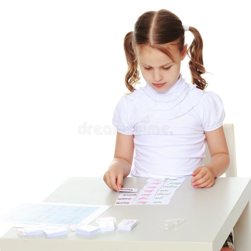 Lite studerar flickan Montessori material. Lite sitter studerar flickan i det Montessori dagiset på en tabell och Montessori material Begreppet av skolan och förskole- utbildning, harmonisk utveckling av barnet bakgrund isolerad white