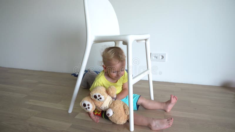 Liten blond babypojke som leker med teddybjörn som sitter under stol. gimbal motion