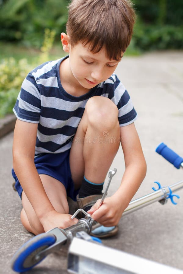 Liten caucasian pojke som reparerar sparkcykeln arkivfoton