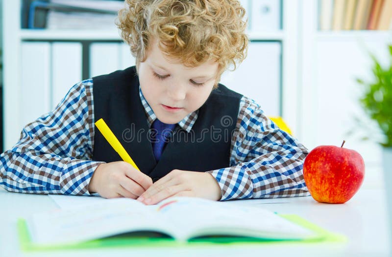 Liten Caucasian skolpojkehandstil i ett anteckningsboksammanträde på en tabell Det röda äpplet ligger bredvid tabellen Time för l