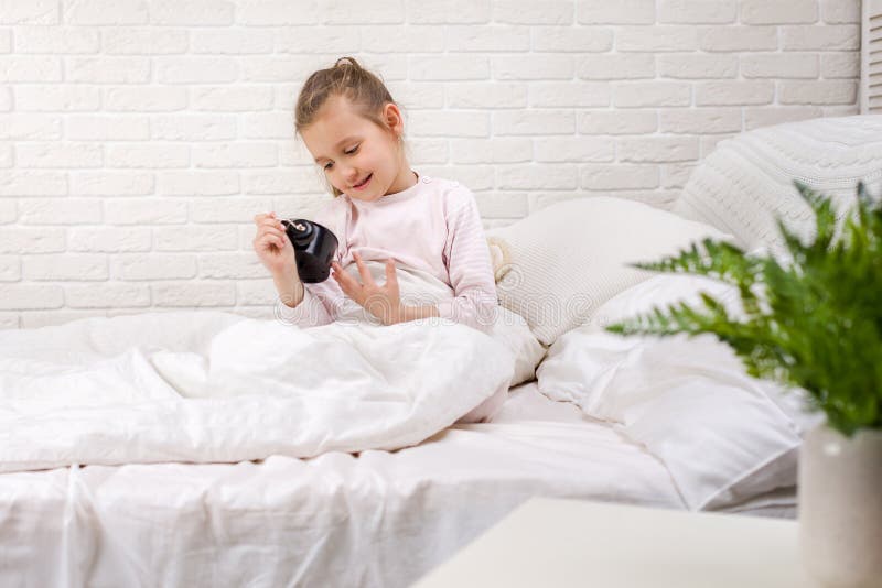 Liten flicka i pyjamas med klockan. Cute little child girl in pyjamas with clock in bed. good morning