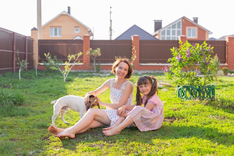 Liten flicka i rosa klänning med sin mor och jack russell skräckhund på gården som sitter på gräset royaltyfria foton