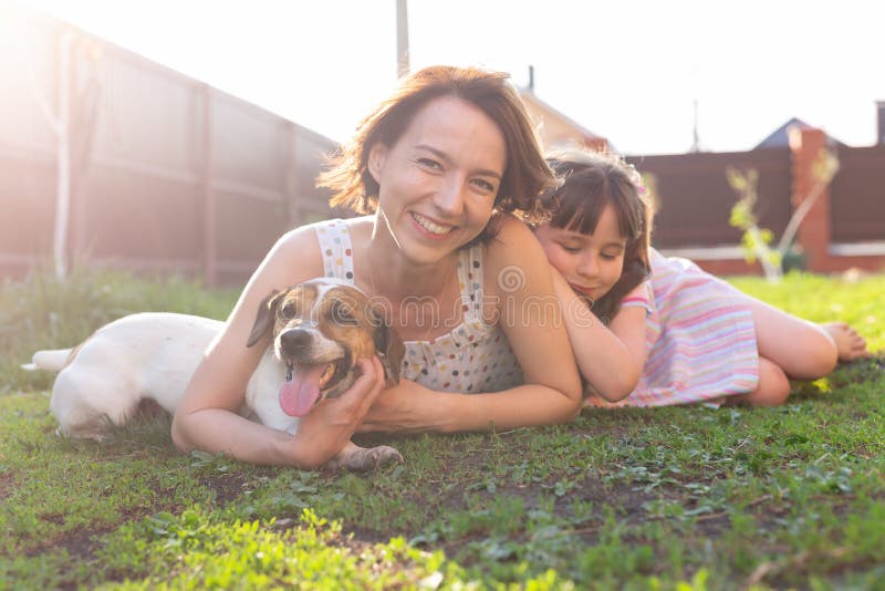 Liten flicka i rosa klänning med sin mor och jack russell skräckhund på gården som sitter på gräset arkivbilder