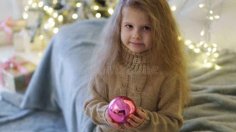 Liten flicka med julleksaken. Lilla flickan är den hållande skinande glass bollen i henne händer Leksak för att dekorera julgranen lycklig barndom