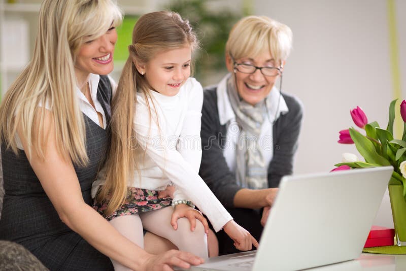Liten flicka som använder bärbara datorn med modern och farmodern royaltyfri foto Liten flicka som använder bärbara datorn med modern och farmodern royaltyfri foto