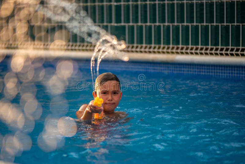 Liten flicka som har kul att leka vattenpistol och simma i poolen