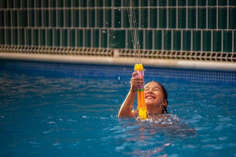 Liten flicka som har kul att leka vattenpistol och simma i poolen