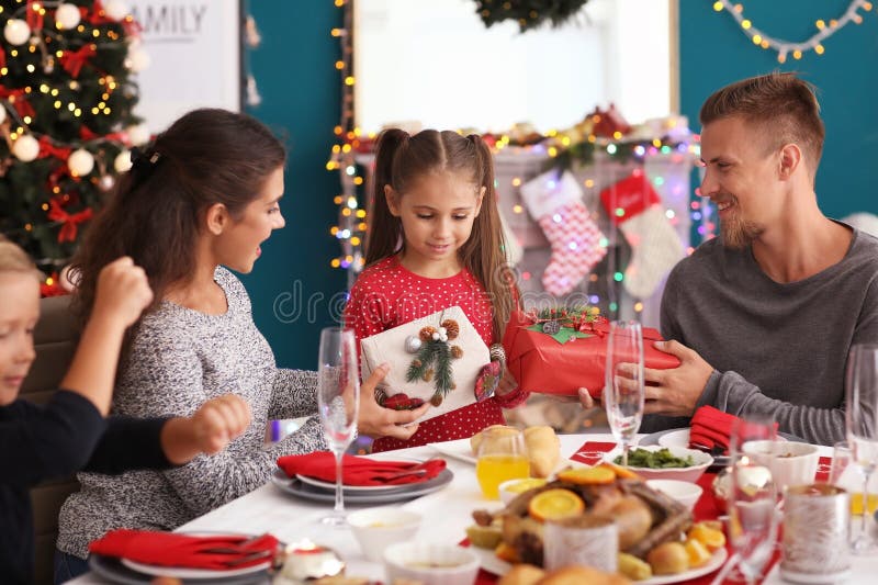 Liten flicka som mottar gåvor från henne föräldrar under julmatställe fotografering för bildbyråer Liten flicka som mottar gåvor från henne föräldrar under julmatställe fotografering för bildbyråer