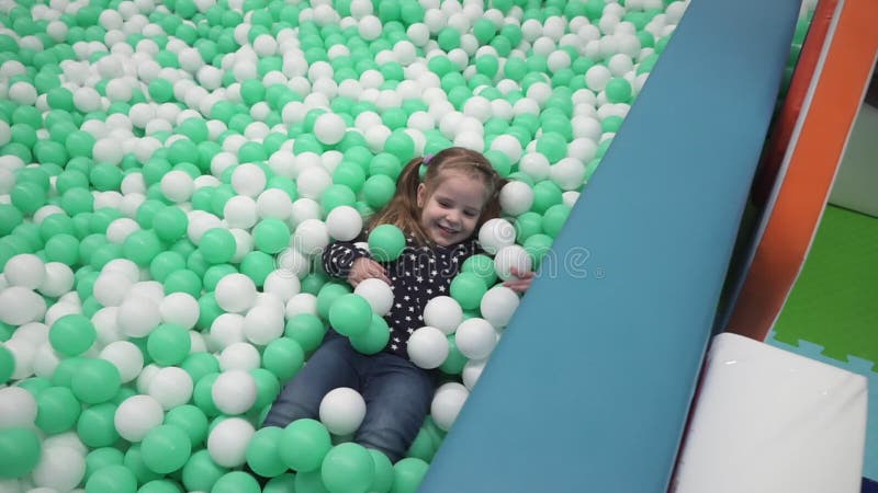 Liten flicka som spelar med små bollar på lekplats i barns mitt