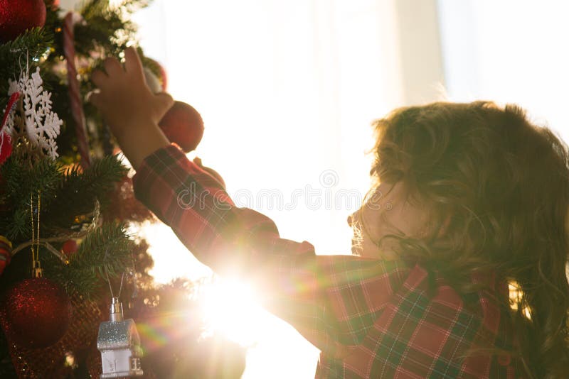 Liten flickabarnet dekorerar en julgran mot fönstret w fotografering för bildbyråer Liten flickabarnet dekorerar en julgran mot fönstret w fotografering för bildbyråer