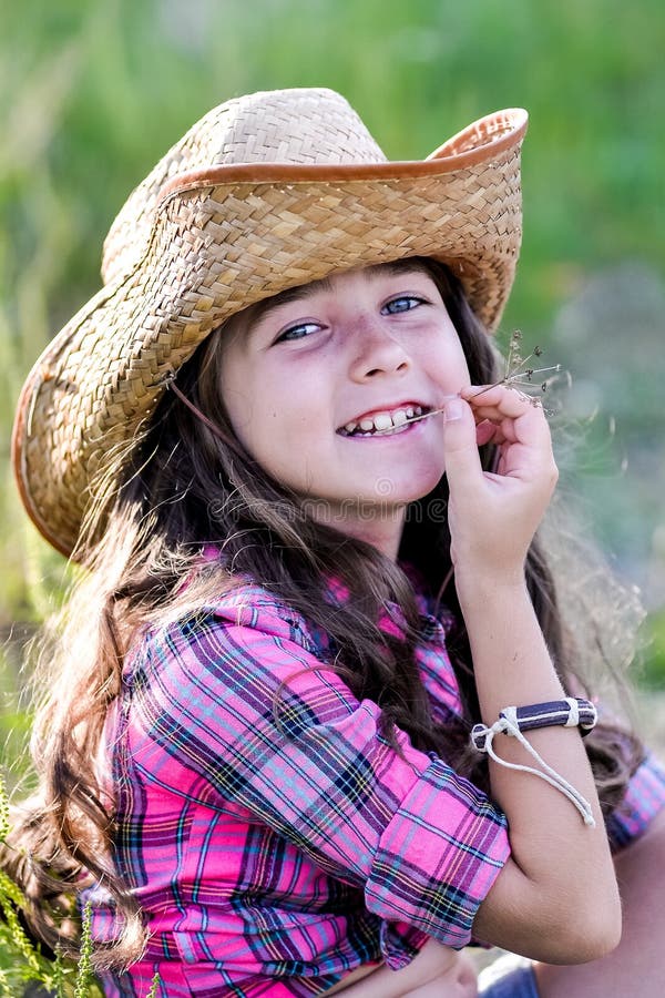 Liten flickasammanträde i ett fält som bär en cowboyhatt arkivbild Liten flickasammanträde i ett fält som bär en cowboyhatt arkivbild