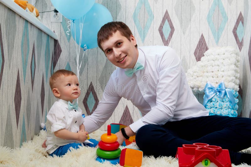 Small cute male child with father on the floor with toys during a photo shoot in the room in 1 year. Small cute male child with father on the floor with toys during a photo shoot in the room in 1 year