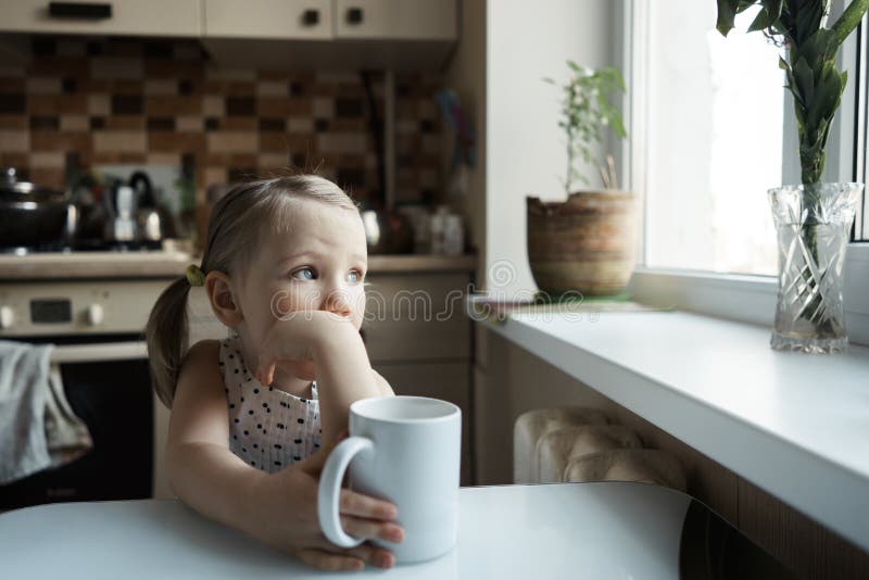 Liten gullig flicka som sitter på tabellen i köket fotografering för bildbyråer Liten gullig flicka som sitter på tabellen i köket fotografering för bildbyråer