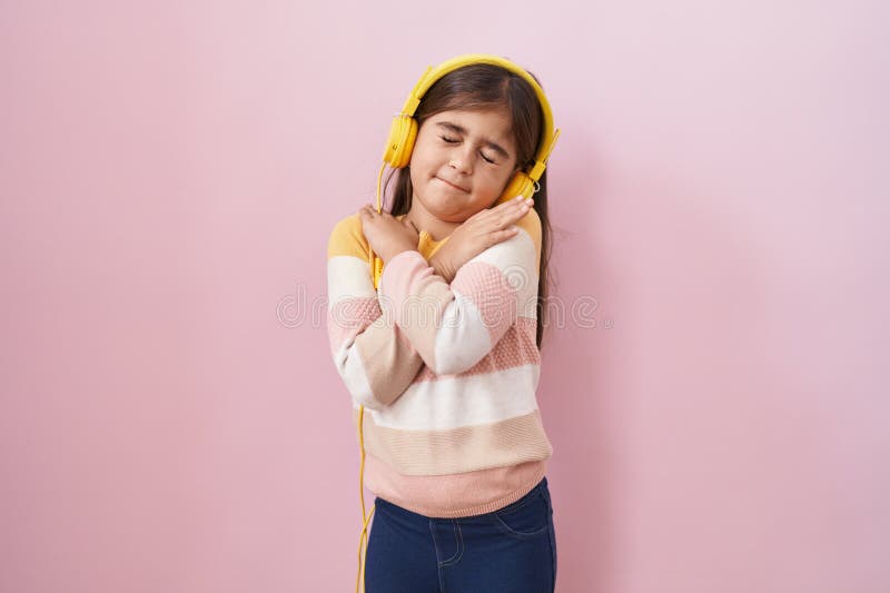 Liten historisk flicka som lyssnar på musik med hörlurar som kramar sig själv, glad och positiv, leende självsäker royaltyfri foto