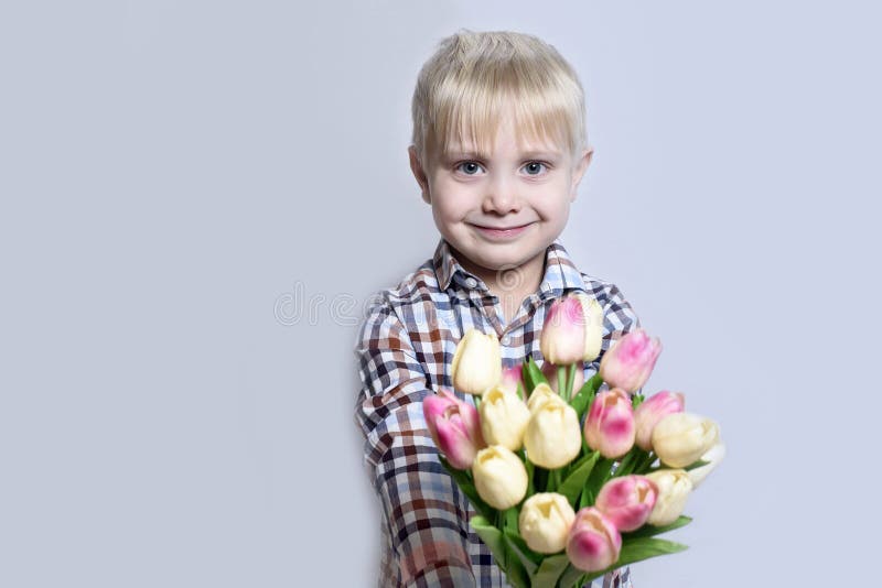 Liten le blond pojke som rymmer en bukett av tulpan ljus stående för bakgrund royaltyfri fotografi Liten le blond pojke som rymmer en bukett av tulpan ljus stående för bakgrund royaltyfri fotografi