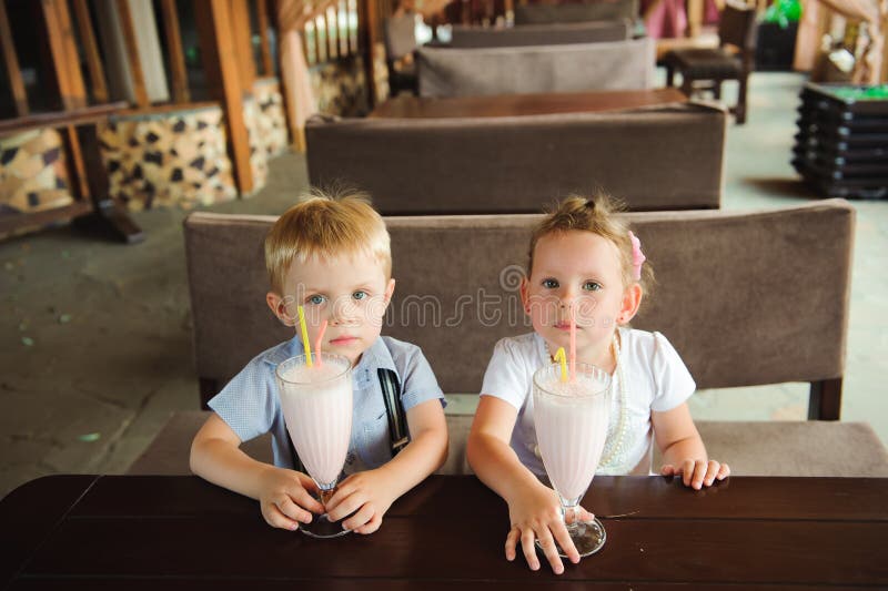 Liten pojke och flicka som dricker mjölkshakes i en café utomhus. royaltyfri fotografi