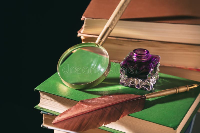 Literature concept. Inkstand with feather near magnifying glass on old books against black background stock photo Literature concept. Inkstand with feather near magnifying glass on old books against black background stock photo