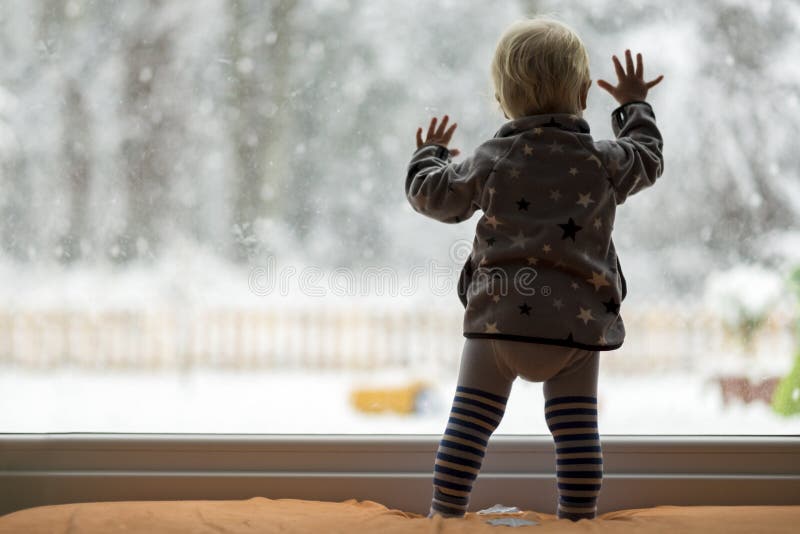 Litet barnbarn som framme står av en stor fönsterbenägenhet mot arkivfoton