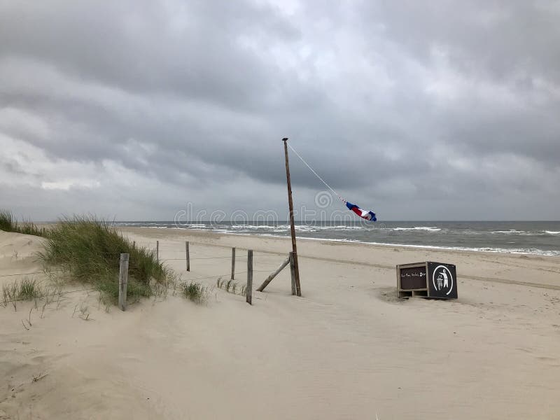 litoral vazio em um Mar do Norte holandês em um dia tormentoso, ventoso, cinzento bandeira que acena no mastro de bandeira imagens de stock litoral vazio em um Mar do Norte holandês em um dia tormentoso, ventoso, cinzento bandeira que acena no mastro de bandeira imagens de stock