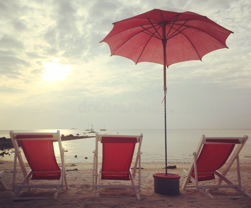 Lits et parapluie rouges de plage sur le coucher du soleil blanc de plage image libre de droits Lits et parapluie rouges de plage sur le coucher du soleil blanc de plage image libre de droits
