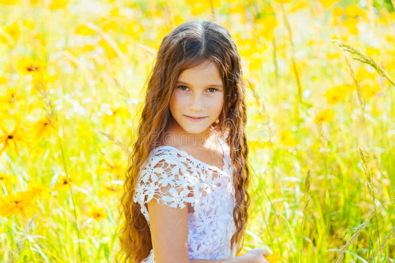 Little girl with long hair in a white dress rejoices in a field with flowers