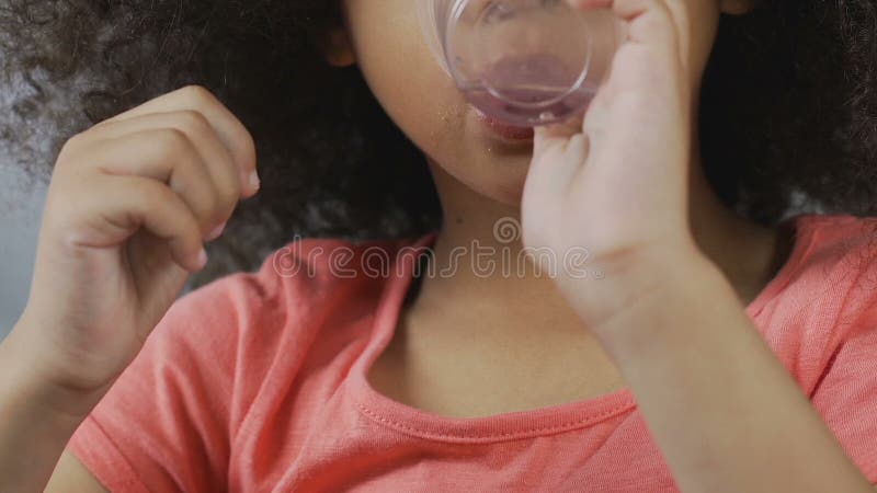 Little african-american girl drinking clear water from plastic glass, beverage