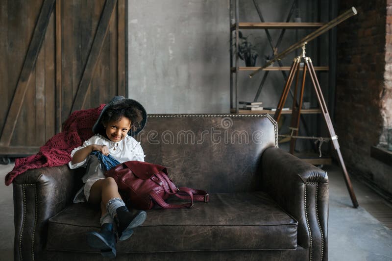 Little african american kid girl puts things in a red leather backpack stock photo