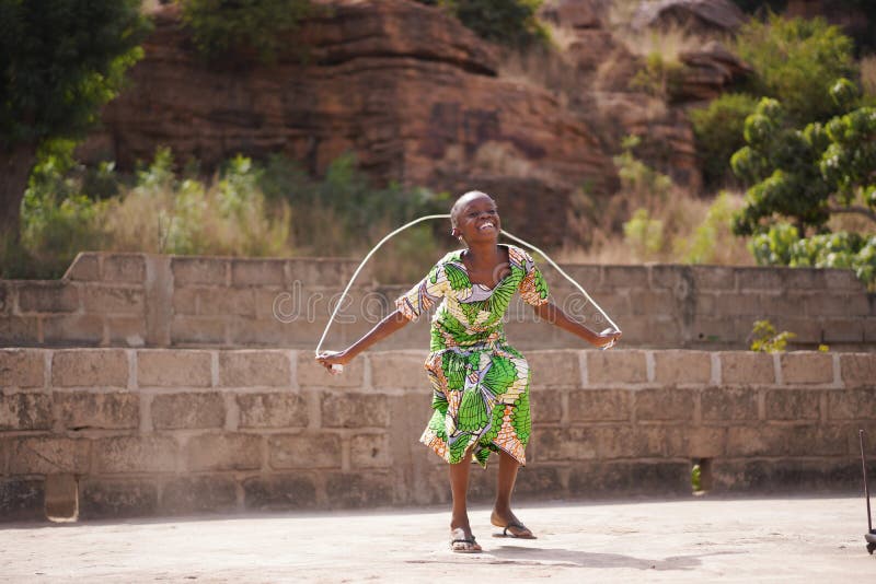 Little African Girl Enjoying Herself With Her Skipping Rope, candid photo of real African children in a natural village environment