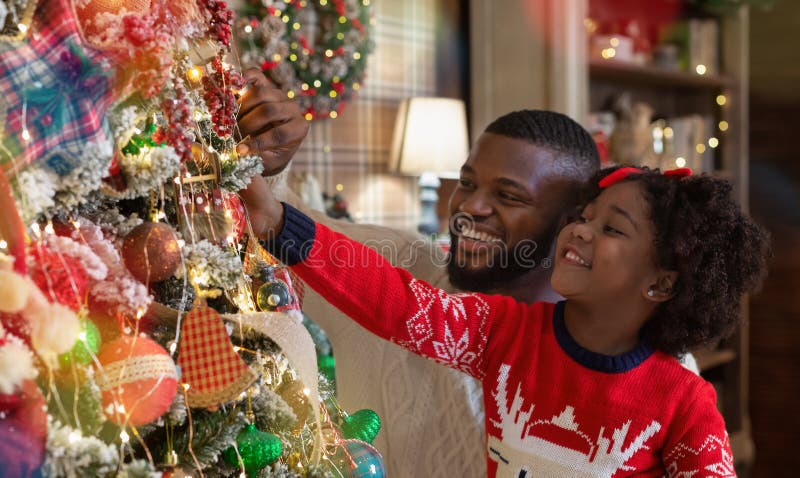 Little afro girl helping daddy to decorate family Christmas tree