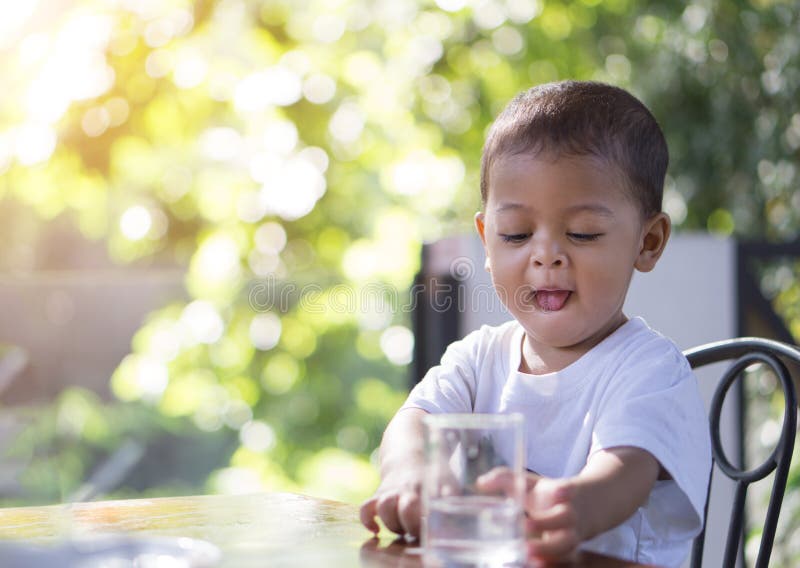 Little asian baby going to drink water in a glass cup in the morning time with bokeh background.