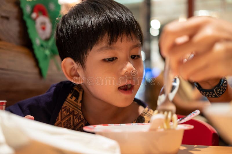 A little Asian boy is eating while his mother feeds him stock photos