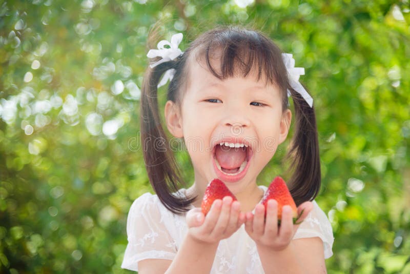 Girl holding strawberries and smiles between picnic. Little asian girl holding strawberries and smiles between picnic in park royalty free stock image Girl holding strawberries and smiles between picnic. Little asian girl holding strawberries and smiles between picnic in park royalty free stock image