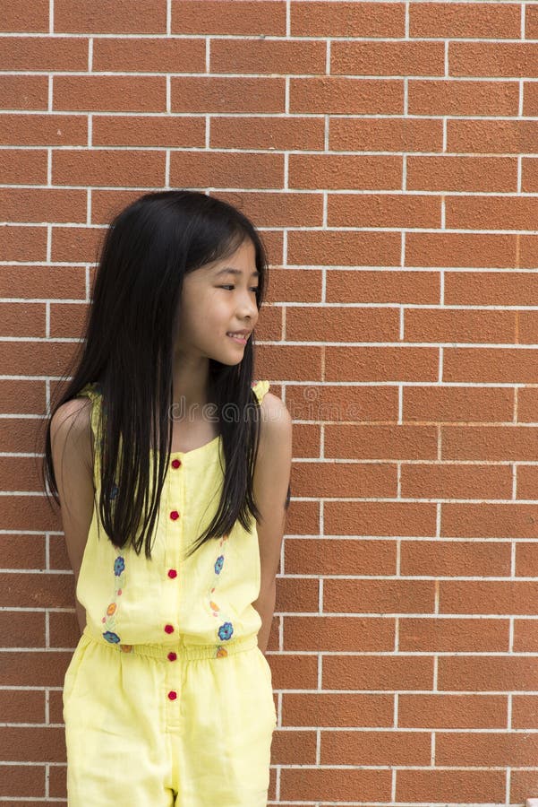 Little Asian girl portrait against brick wall.