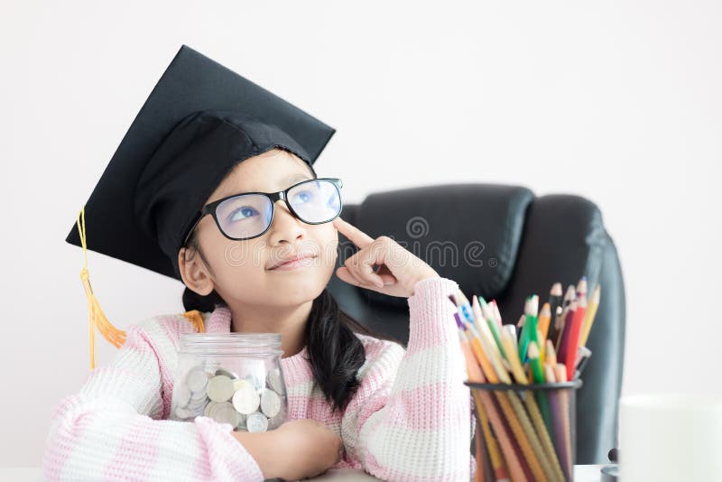 Little Asian girl wearing graduate hat hugging clear glass jar piggy bank and smile with happiness for money saving to wealthness