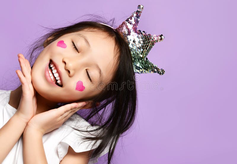 Asian Korean kid girl princess in crown closeup portrait Happy smiling laughing with a painted red hearts sign on cheeks stock photos Asian Korean kid girl princess in crown closeup portrait Happy smiling laughing with a painted red hearts sign on cheeks stock photos