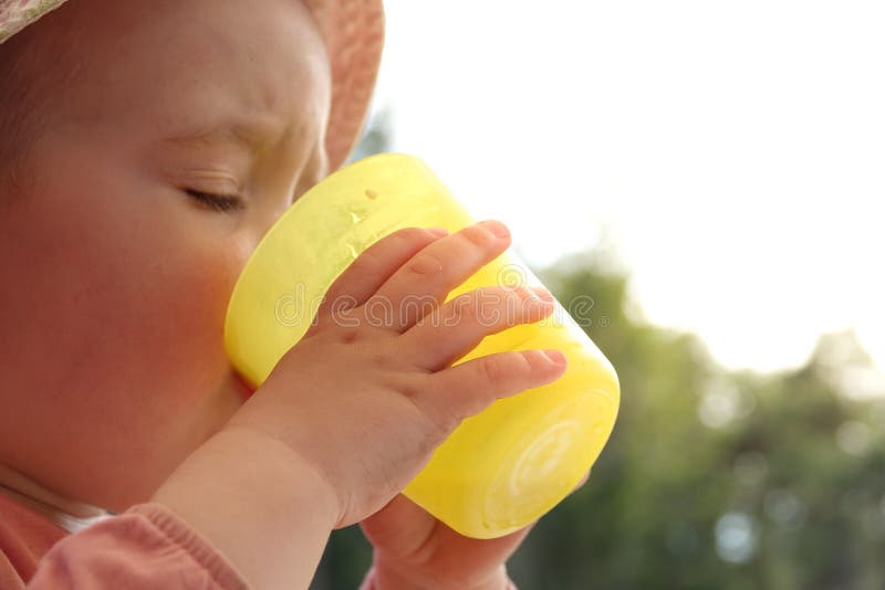 A little baby girl drinks water from a plastic glass