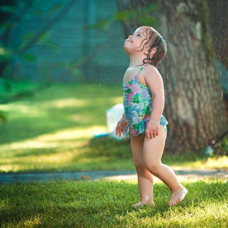 The little baby girl playing with garden sprinkler.