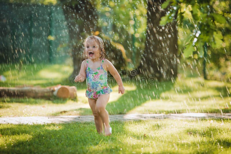 The little baby girl playing with garden sprinkler.