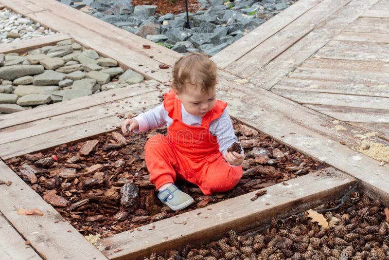 Little baby girl in a red suit studies natural materials bumps, bark, stones, pine cones. Caucasian child sits on the ground stock photos Little baby girl in a red suit studies natural materials bumps, bark, stones, pine cones. Caucasian child sits on the ground stock photos