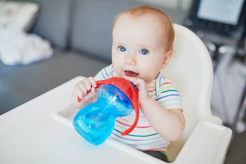 Little baby girl sitting in high chair and drinking water from sippy cup