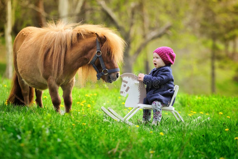 Little baby girl on wooden rocking horse and pony