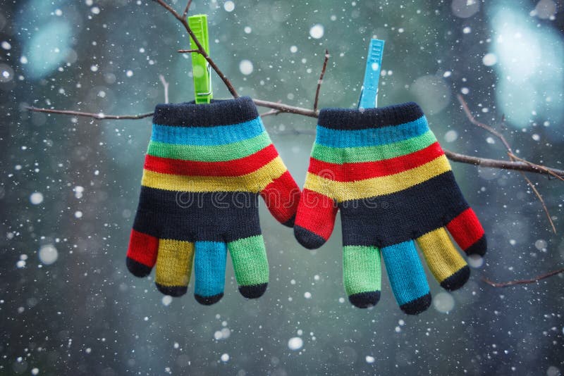 Little baby gloves hanging by a thread in winter day under the falling snow.